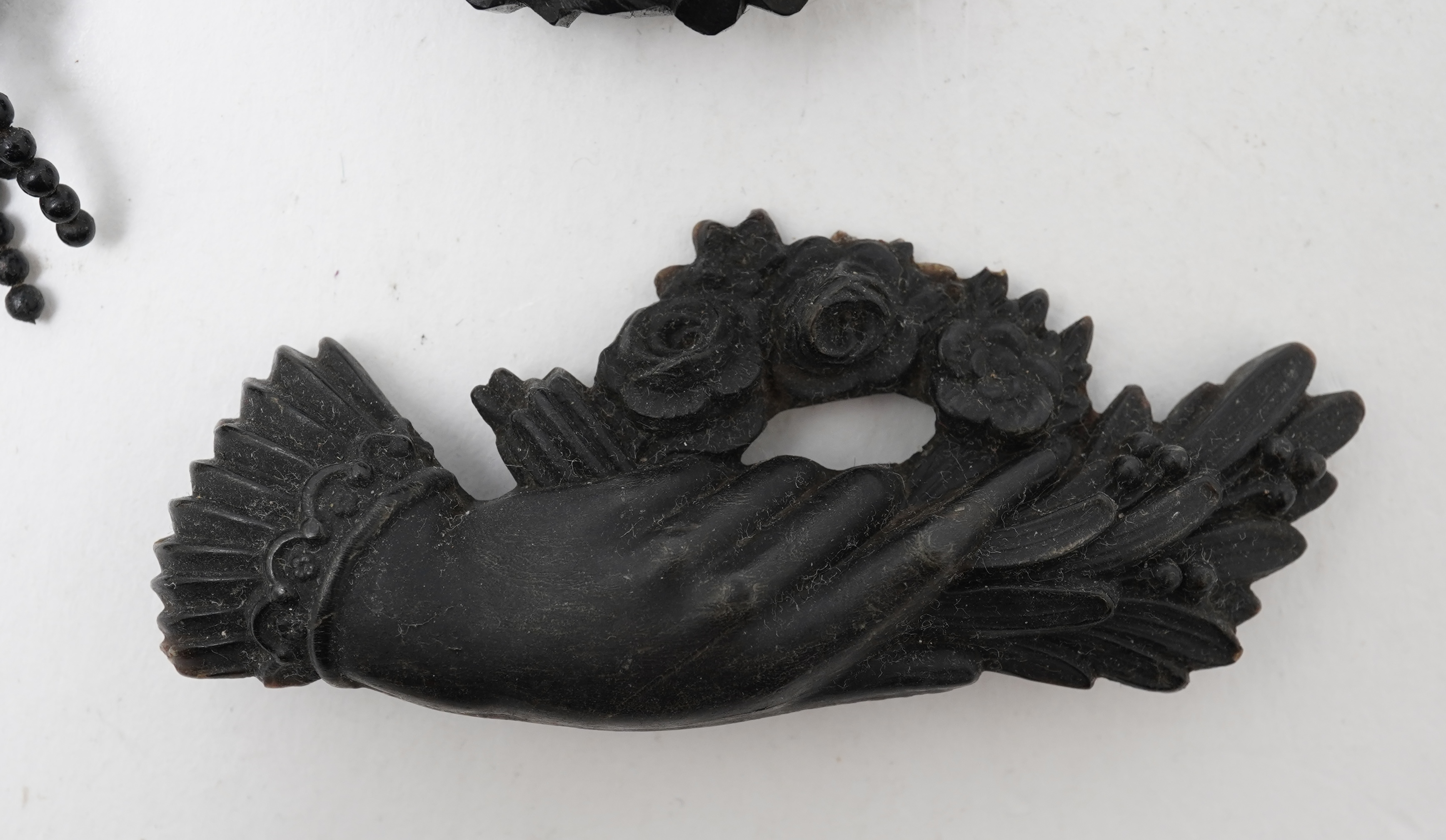 A collection of jewels, comprising: a moulded bog oak brooch depicting a hand holding a posy, length 7.4cm; a carved jet brooch depicting a Gothic ruin, possibly part of Whitby Abbey; a necklace composed of polished pane